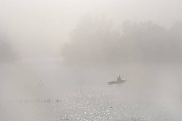 Novi Sad, Serbia - October 30, 2014: Man in a boat fishing at river Danube. Cold morning scene with mist covered landscape.