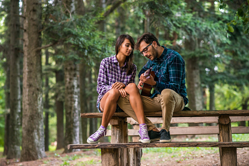 Man playing a guitar to his girlfriend in a park.