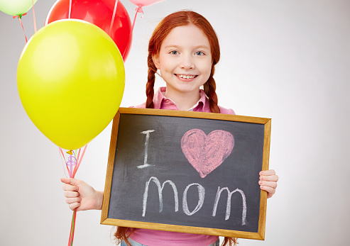 Charming girl holding balloons and blackboard with love declaration to her mom