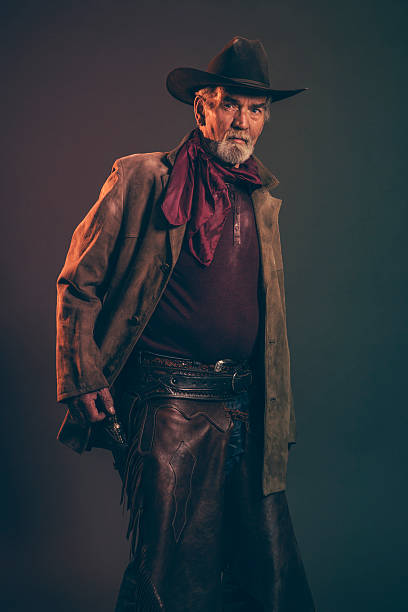 istock Senior cowboy with gray beard and brown hat pulling revolver. 521384347