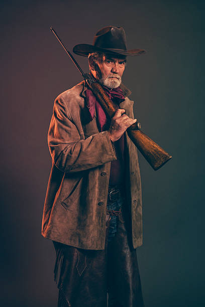 istock Senior cowboy with gray beard and brown hat holding rifle. 521384353