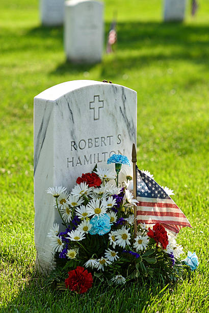 Tombstone, Flowers, Arlington National Cemetery, Close-up Arlington, Virginia, USA - May 24, 2015: Close-up of a Christian tombstone with flowers and a U.S. flag at Arlington National Cemetery. arlington cemetery in spring stock pictures, royalty-free photos & images