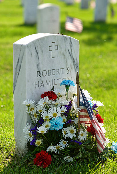 Tombstone, Flowers, Arlington National Cemetery, Close-up Arlington, Virginia, USA - May 24, 2015: Close-up of a Christian tombstone with flowers and a U.S. flag at Arlington National Cemetery. arlington cemetery in spring stock pictures, royalty-free photos & images