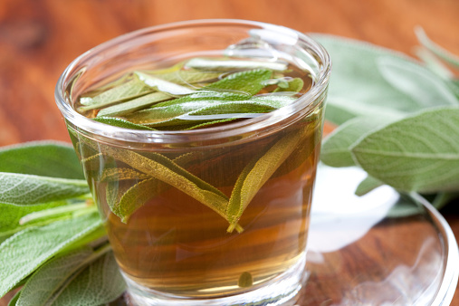 sage tea with fresh leaf inside teacup and bunch of sage around, on wooden floor, closeup, half aerial view,