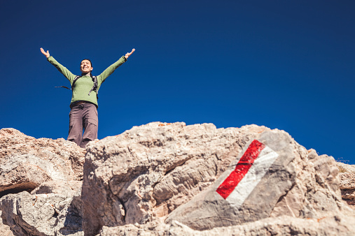 Woman on mountain peak with arm raised in a sense of freedom during a beautiful day.