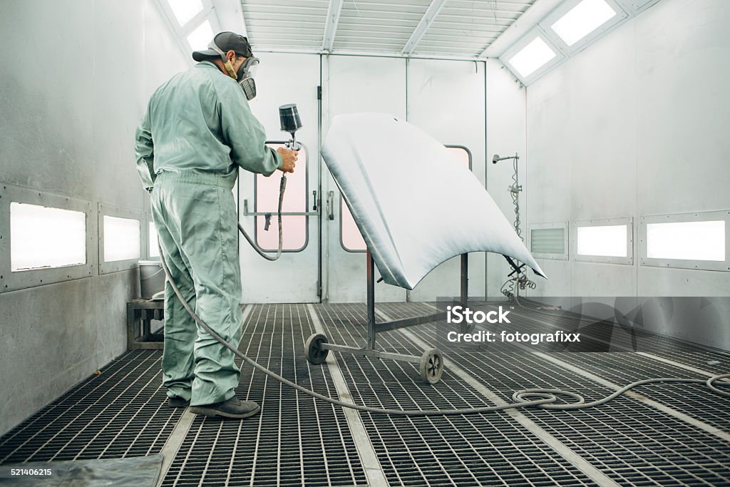 mechanic in Painting Booth spray the hood of a car Spray Painter in Protective Workwear spray a hood of car Car Stock Photo