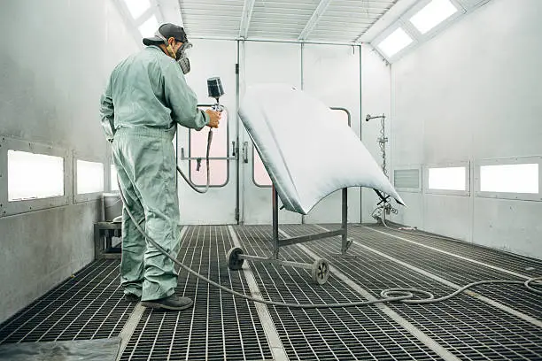 Photo of mechanic in Painting Booth spray the hood of a car