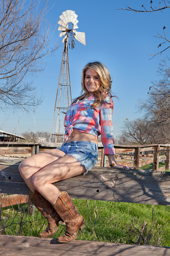 Cowgirl sitting on fence with windmill in background