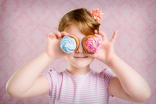 Little girl holding cupcakes in hands covering eyes