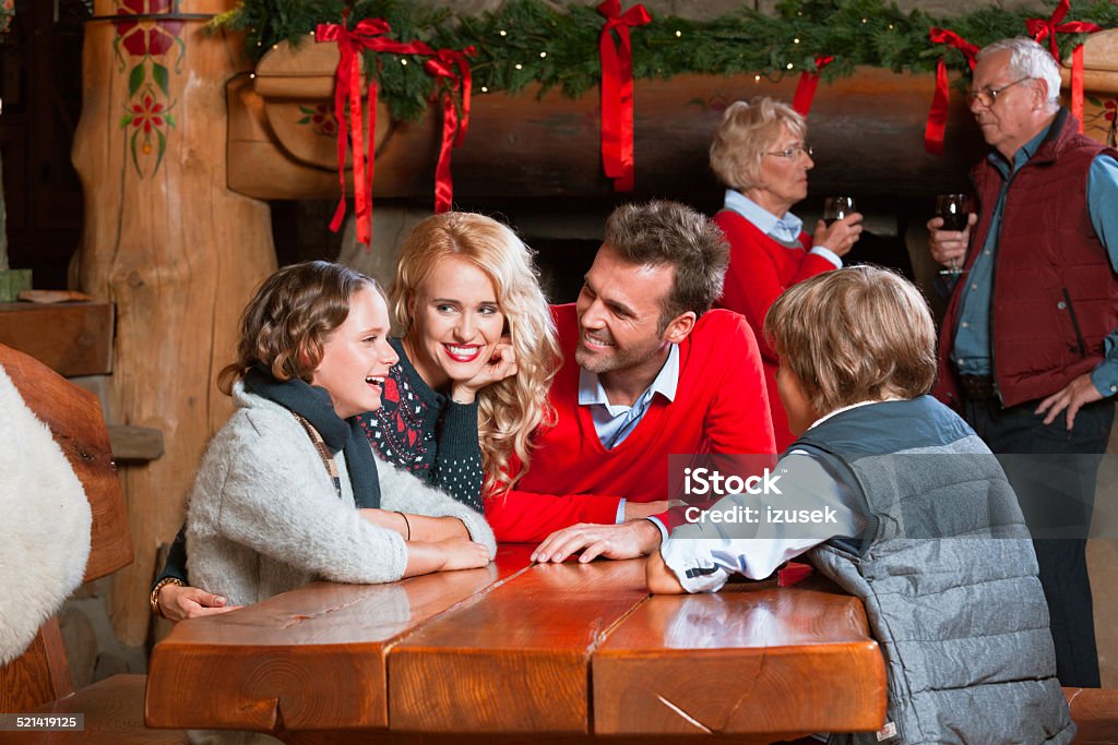 Happy family meeting at Christmas Time Happy parents talking with their children at the table at home with granparents drinking re wine by the fireplace decorated with christmas ornaments. Christmas Stock Photo