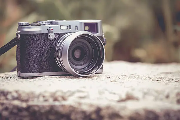 Vintage-style digital camera on boulder over blurred nature background. Shallow depth of field with focus on camera. Outdoor. Retro picture style.