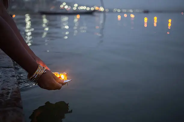 A evening shot of a woman putting blessed puja flowers in the river Ganges in Varanasi, India