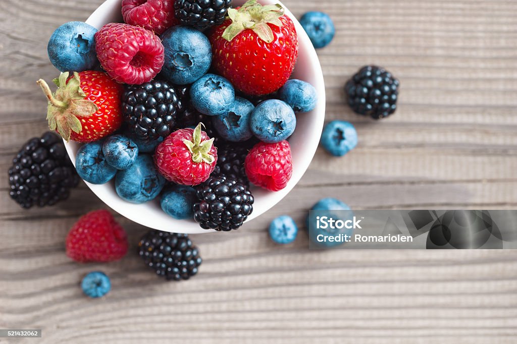 Fresh berries in a basket on rustic wooden background. Fresh berries in a basket on rustic wooden background. Close up, top view, high resolution product. Harvest Concept Berry Fruit Stock Photo