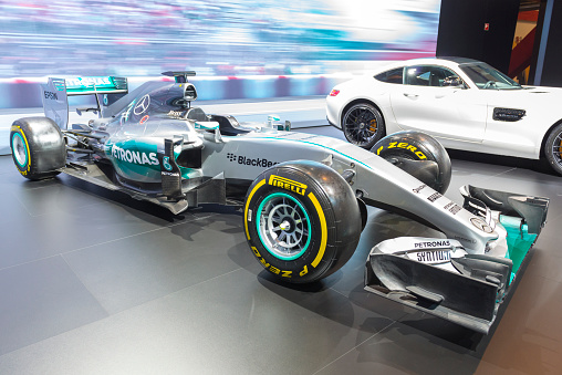 Brussels, Belgium - Januari 12, 2016: The 2015 championship winning Mercedes F1 W06 Hybrid race car of Lewis Hamilton and Nico Rosberg. A white Mercedes-AMG GT coupe performance  sports car is on display in the background. The car is on display during the 2016 Brussels Motor Show. The car is displayed on a motor show stand, with lights reflecting off of the body. There are people looking around and other cars on display in the background.