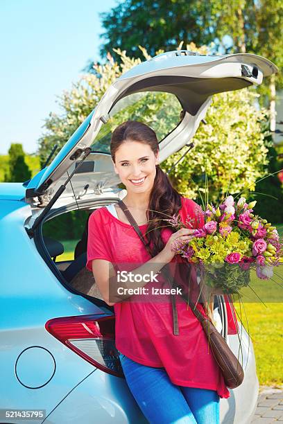 Young Woman Standing Outdoor By Car Holding Flowers Stock Photo - Download Image Now