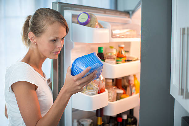 Pretty, young woman in her kitchen by the fridge Is this still fine? Pretty, young woman in her kitchen by the fridge, looking at the expiry date of a product she took from her fridge - obsolescence stock pictures, royalty-free photos & images