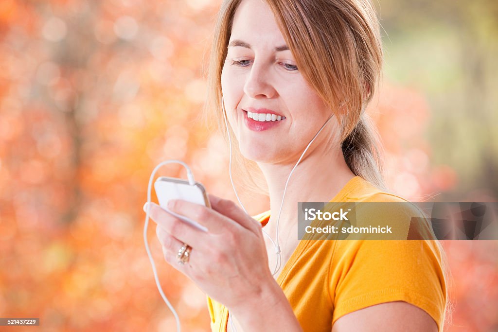 Woman Outdoors In Fall Listening To Music A smiling woman listening to music on her smart phone as she enjoys a beautiful fall day outdoors. 40-44 Years Stock Photo