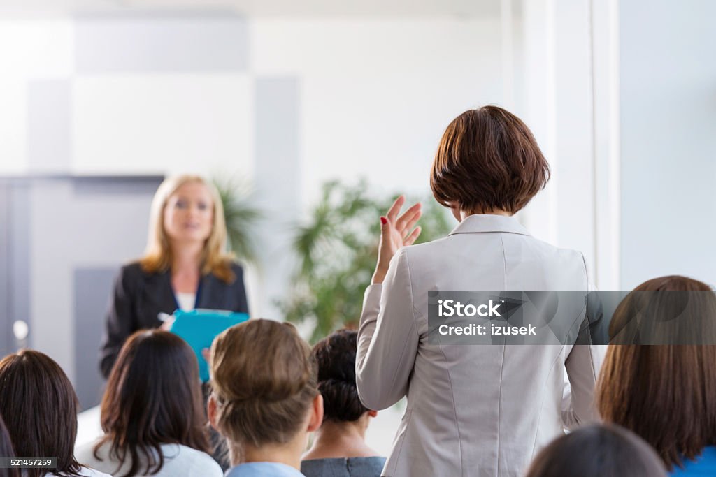 Businesswoman asking a question during seminar Back view of group of businesswomen attending a seminar. Focus on the woman asking a question the female coach. Women Stock Photo