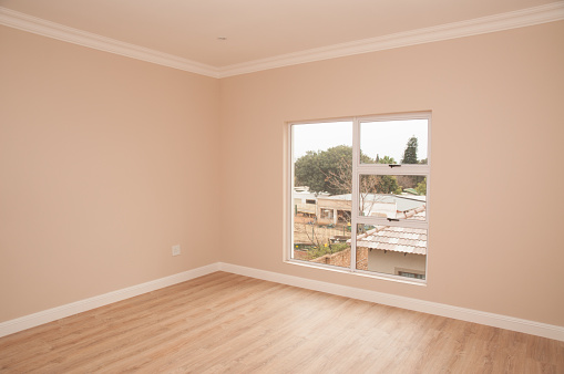 The interior of an empty bedroom, looking towards the window over the laminated floor, of a newly build house.