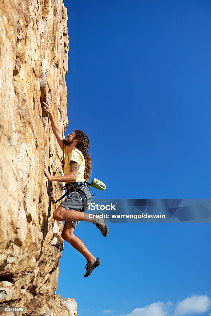 Reaching new heights A rockclimbing man reaching for a grip on a steep mountain in the outdoors Adrenaline Stock Photo