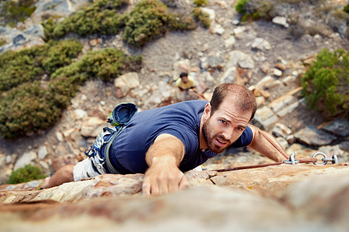A man reaching for a grip while he rock climbs on a steep cliff