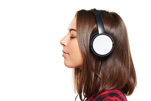 Side view closeup portrait of young female listening enjoying music in headphones with closed eyes, over white background