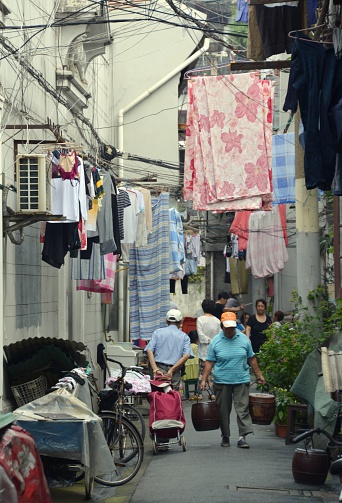 Shanghai, China - September 20, 2014: Local people walking on a narrow street in Shanghai old City, surrounded by hanging drying clothes and sheets. 