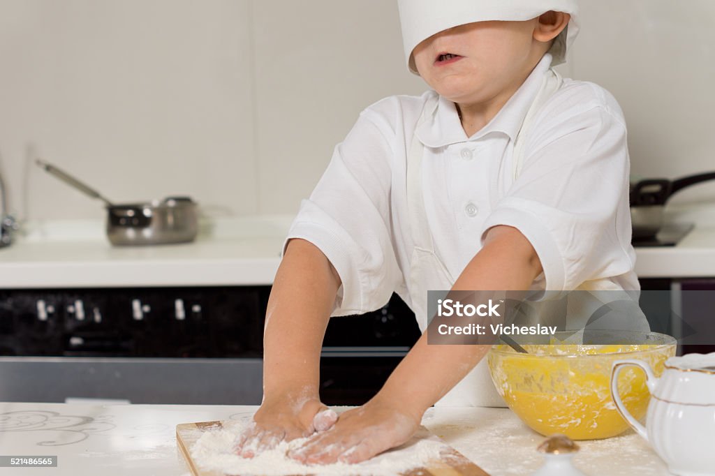 Little child baking in a chefs toque Little child baking in a chefs toque that is falling over his eyes as he rubs his hands in the flour while making pastry Activity Stock Photo