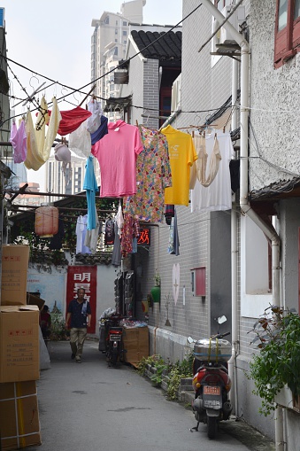 Shanghai, China - September 20, 2014: Chinese man walking on a narrow street, surrounded by hanging drying clothes in Shanghai old City. 