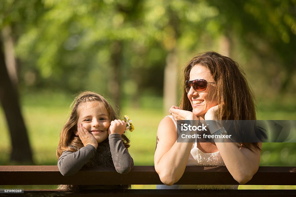 Mother and daughter sitting on a bench Mother and daughter sitting on a bench in the park and playing. Adult Stock Photo