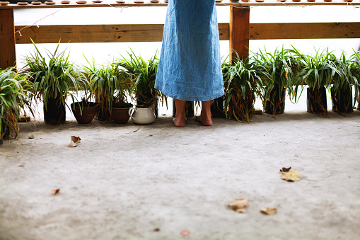 Feet of young thai girl standing at a fence close to many plants in flower pots.