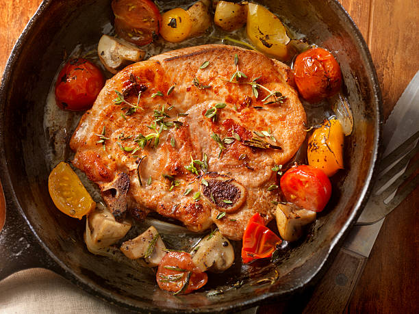 Pork Loin Chops with Tomatoes and Mushrooms Pork Loin Chops with Tomatoes and Mushrooms in a Cast Iron Skillet  -Photographed on Hasselblad H3D2-39mb Camera meat chop stock pictures, royalty-free photos & images