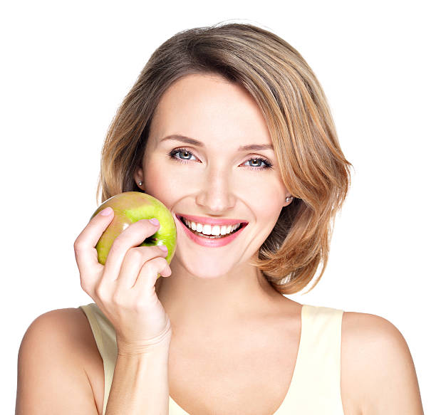 Young beautiful smiling woman touches the apple to face Young beautiful smiling woman touches the apple to face - isolated on white. apple women smiling human teeth stock pictures, royalty-free photos & images
