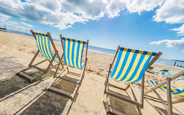 Bournemouth Deck Chairs Angled A row of blue and yellow deck chairs by the beach in Bournemouth. bournemouth england photos stock pictures, royalty-free photos & images