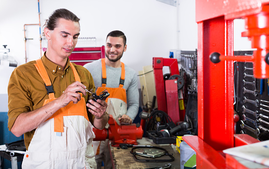 Two workmen toiling in a locksmiths workshop and smiling