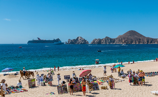 Cabo San Lucas, Mexico- April 27/2016: Vendors sell there wares and services to tourists in front of a resort in Cabo San Lucas as a cruise ship enters the bay.