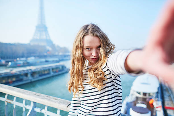 Beautiful young girl taking funny selfie with her mobile phone near the Eiffel tower