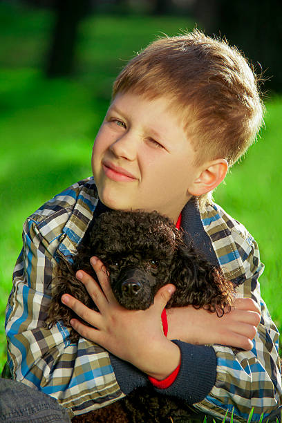 istock Boy sitting on the grass with a black poodle 521534092