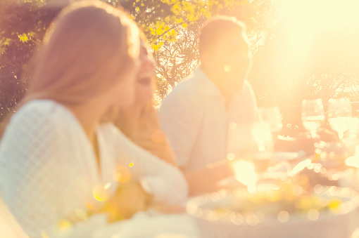 Defocussed group of young people eating outdoors. They are all happy, having fun, smiling laughing and talking. Intentionally shot out of focus