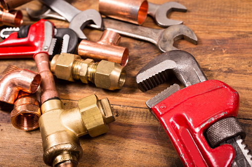 Various construction, DIY, plumber's hand tools and copper and brass plumbing pipes and fittings lie on a rustic wooden table, desk or workbench.  Tools include styles of various wrenches. Home improvement, plumbing, construction themes.  Great background.  Close up.