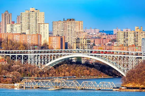 Henry Hudson Bridge spans Spuyten Duyvel Creek, in New York City. Harlem apartment buildings shine under the late afternoon light.