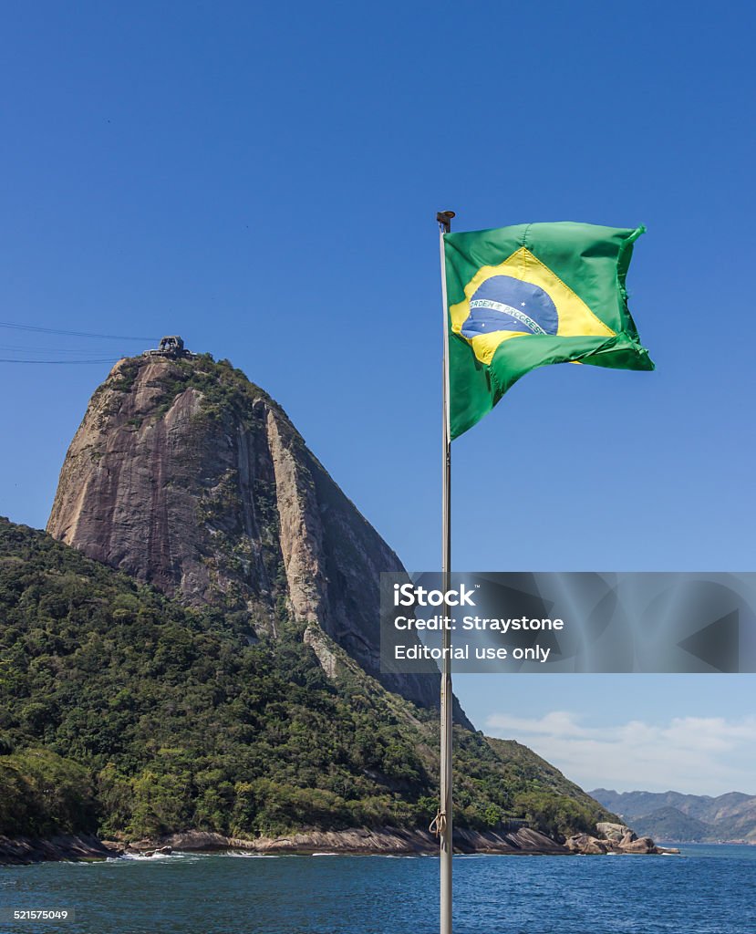 Iconic Brazil Flag of Brazil is flying over Praia Vermelha with Pao de Acucar (Sugarloaf Mountain) in the background. Atlantic Ocean Stock Photo