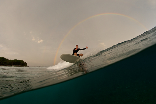 Stoked longboard surfer gives a thumbs up under a rainbow.