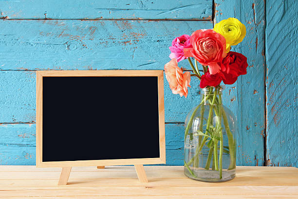 istock flowers next to empty blackboard, on wooden table. copy space 521607292