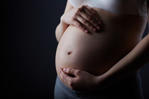 beautiful forty years old pregnant woman with blue shirt isolated on a gray background