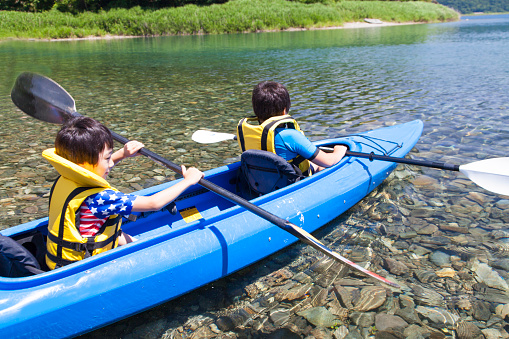 Boys paddling on the tandem kayak in the lake.
