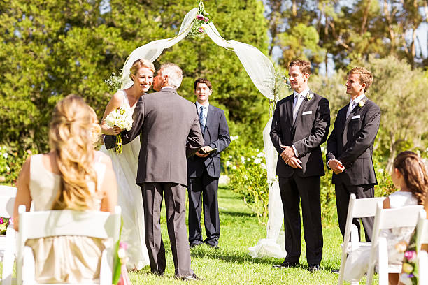 Father Giving Away The Bride At Wedding Ceremony Father kissing bride on cheek with groom and guests looking at them during wedding ceremony. Horizontal shot. bride hugging father on wedding day stock pictures, royalty-free photos & images