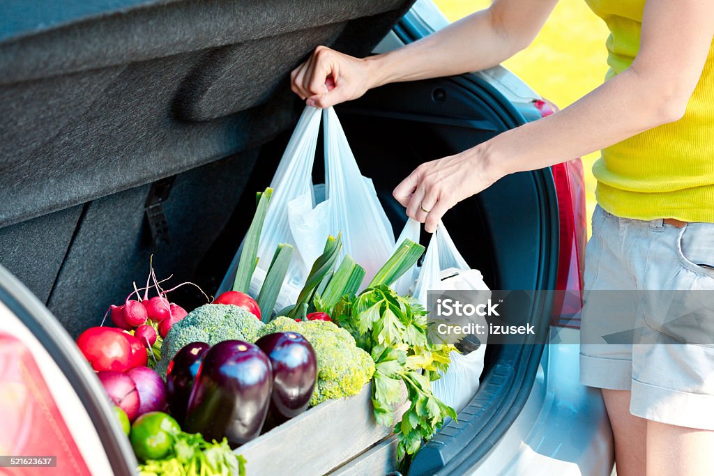 Woman taking out shopping bags from car trunk Woman came back from shopping, standing outdoor by the car trunk and taking out shopping bags. Close up of hands.  Groceries Stock Photo
