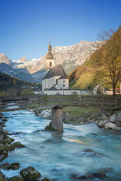 The Church of St. Sebastian in Ramsau / Berchtesgaden in Bavaria. The focus is on the mountain brook "Ramsauer Ache" with the little wooden bridge "Ertlsteg"