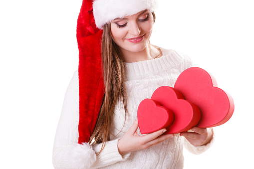 Christmas winter happiness concept. Woman wearing santa helper hat holding many red heart shaped gift boxes isolated on white